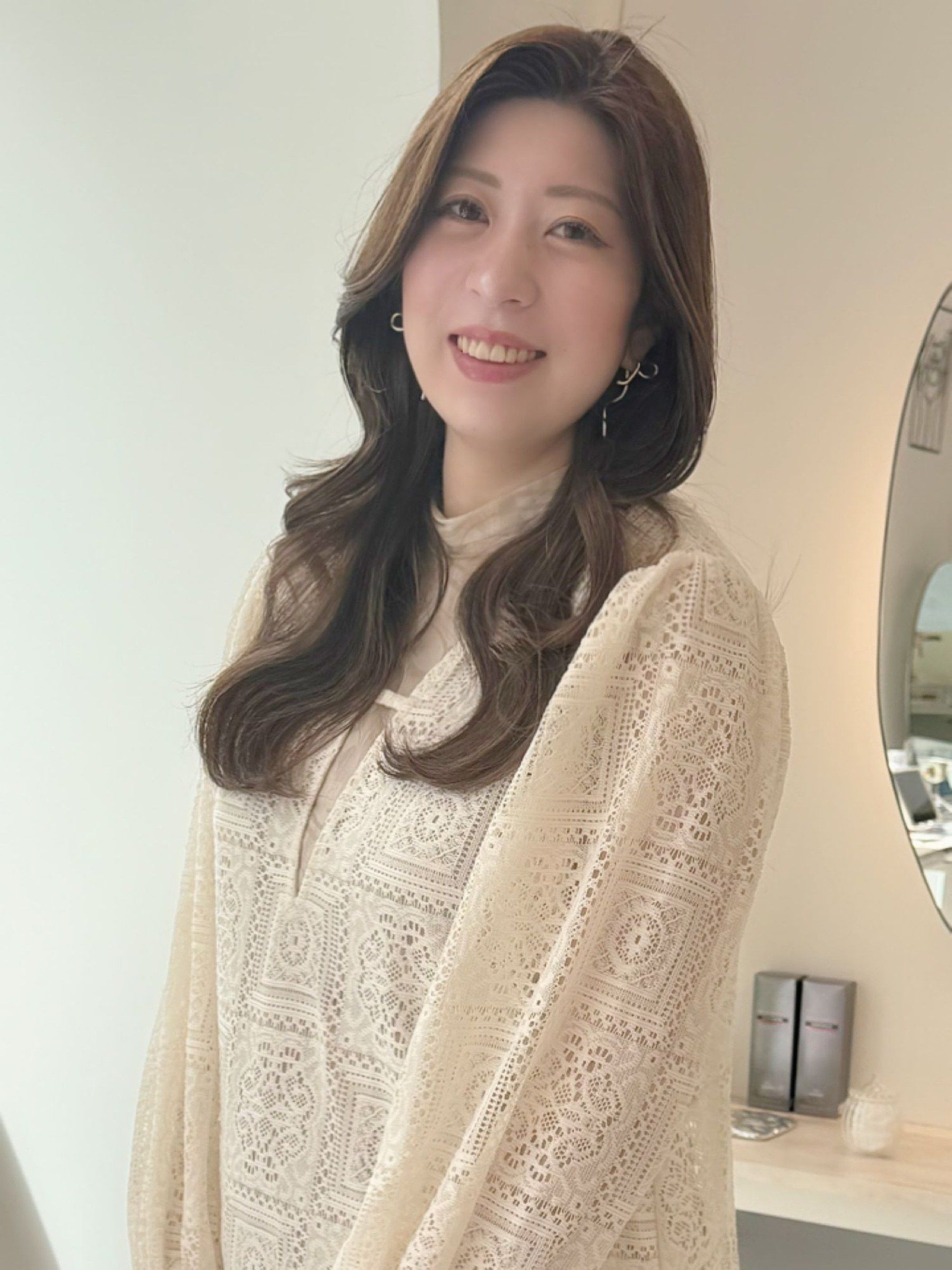 トップスタイリストの玉井香奈。ゆるいウェーブの茶色のロングヘアで、白いレースのブラウスを着ている