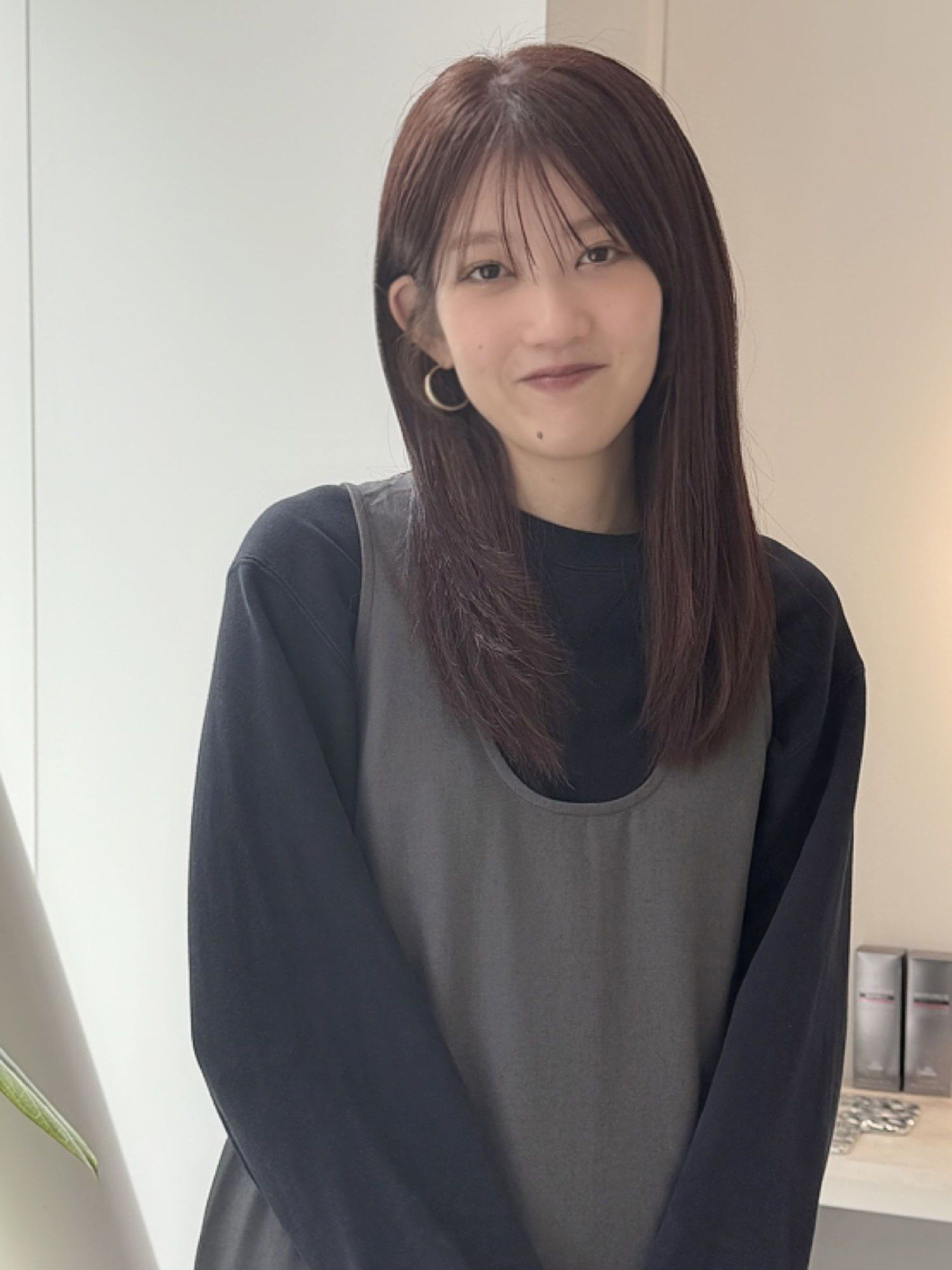 スタイリストのいとう りさ。前髪のある赤みブラウンのストレートロングで、黒のトップスにグレーのベストを重ねている