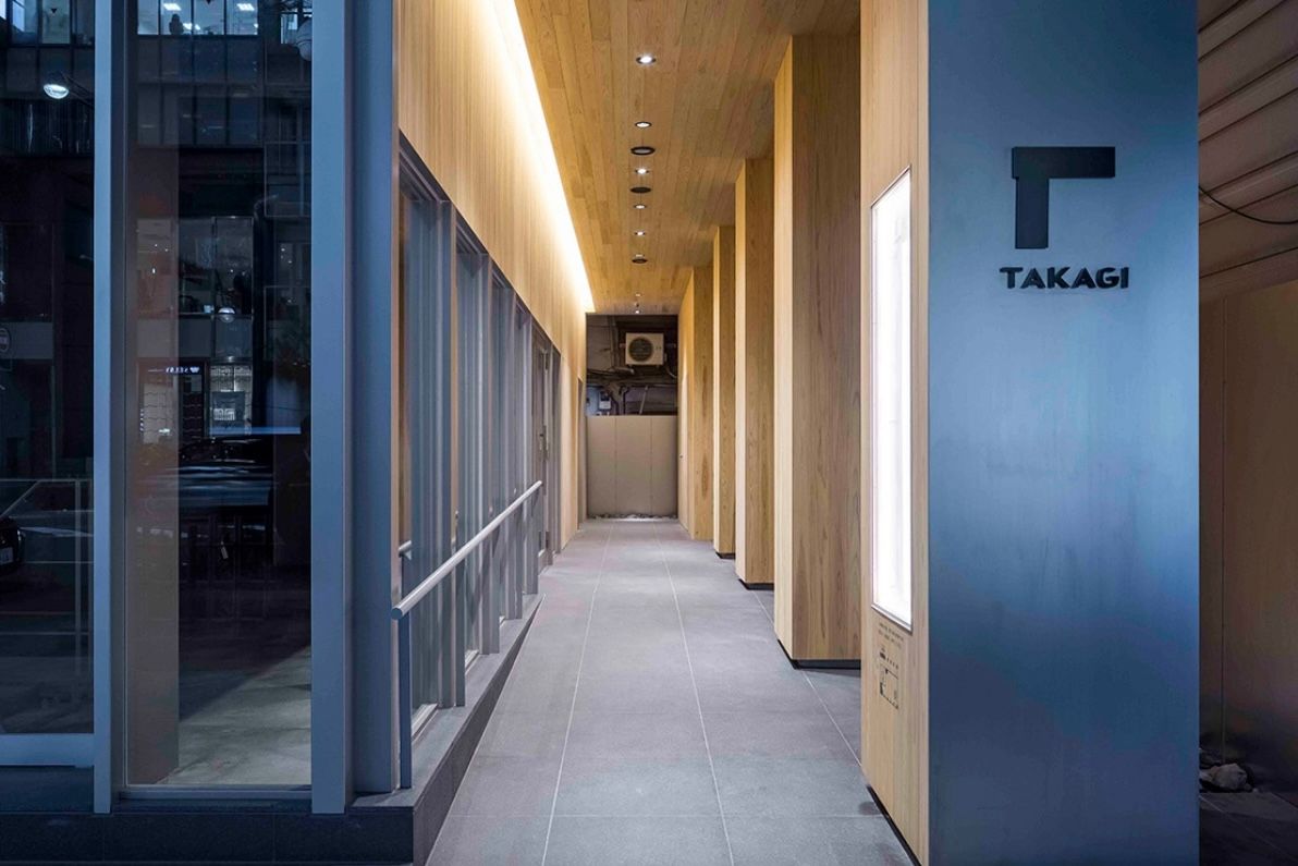 「TAKAGI」のサインがある銀座高木ビルの入口。木の柱が並ぶ通路の奥にエントランスがある