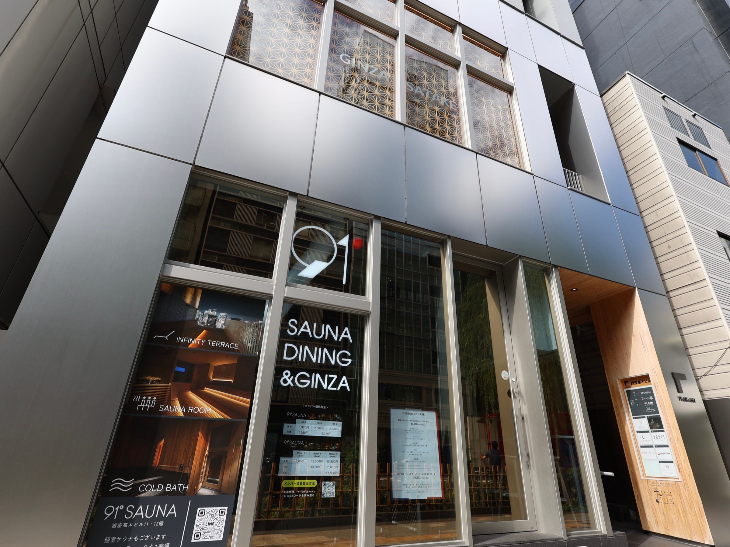 通りから見上げた銀座高木ビルの1階。ガラス張りの店舗と、木目の通路への入口が見える