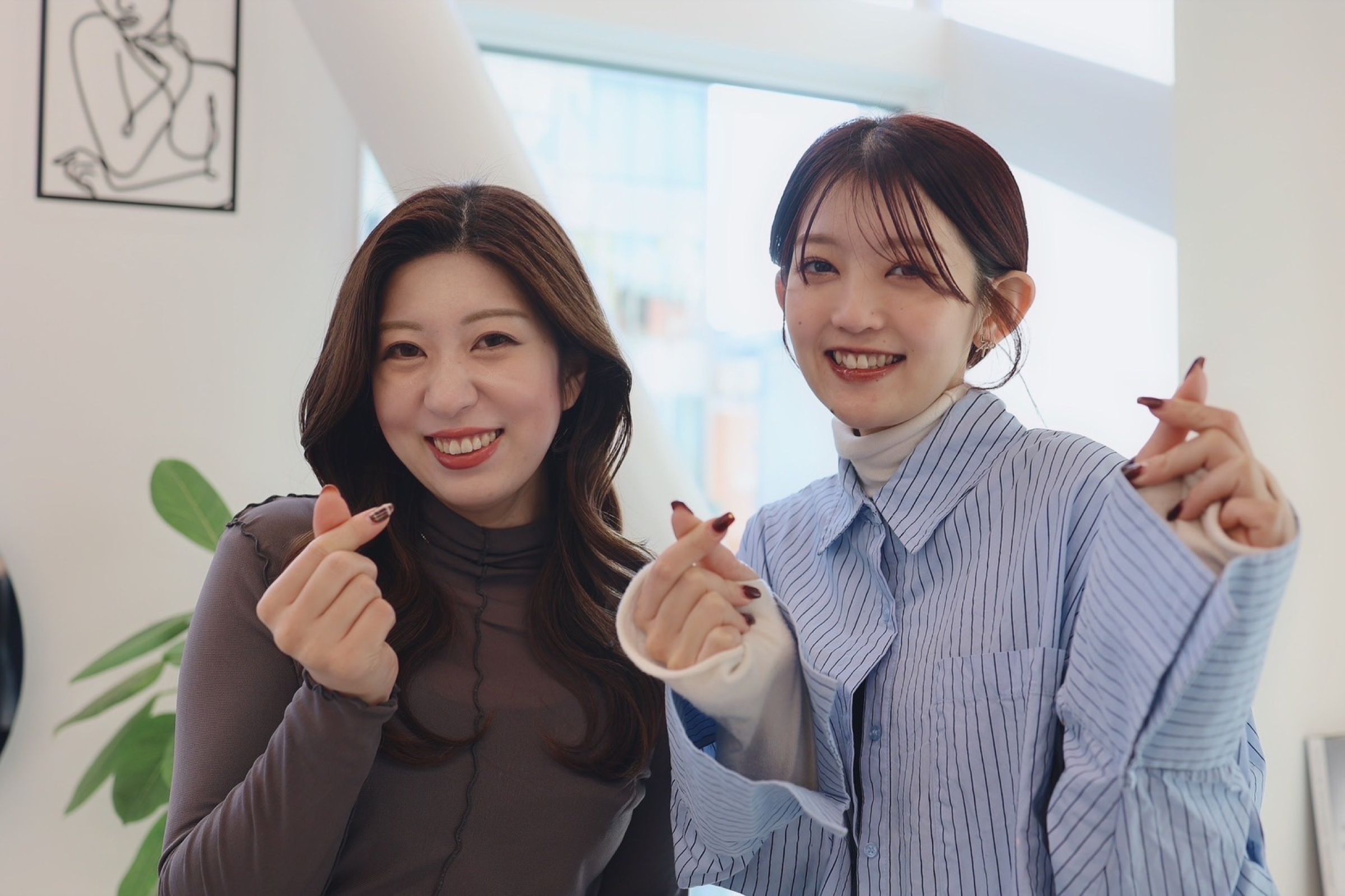 スタッフ2人が並んで、指でハートを作りながら笑っている様子